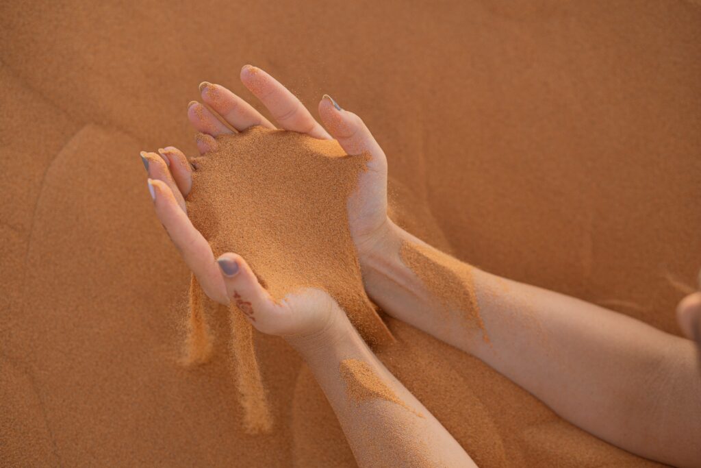 mains qui tiennent du sable orange